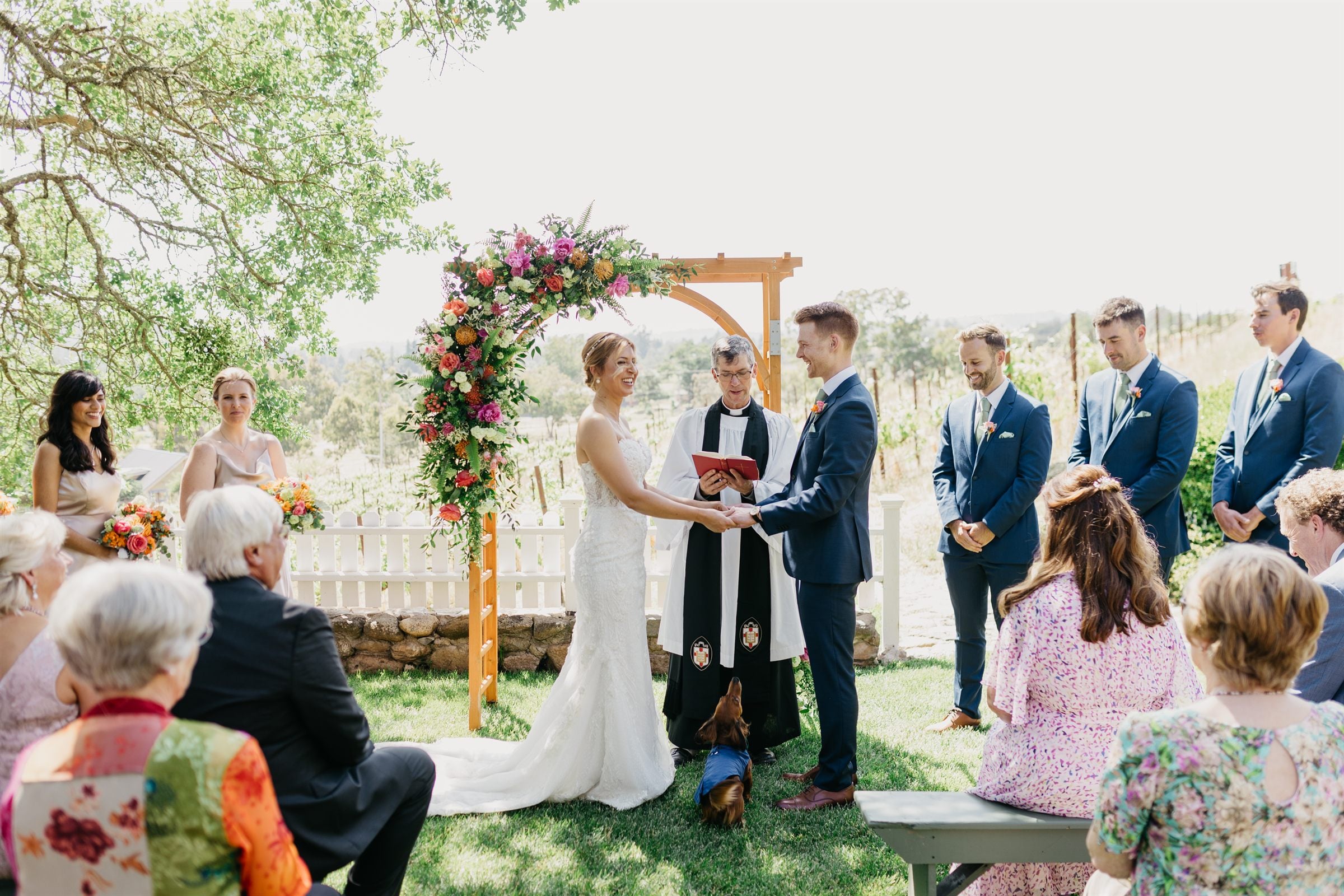 An outdoor wedding ceremony beneath a floral arch