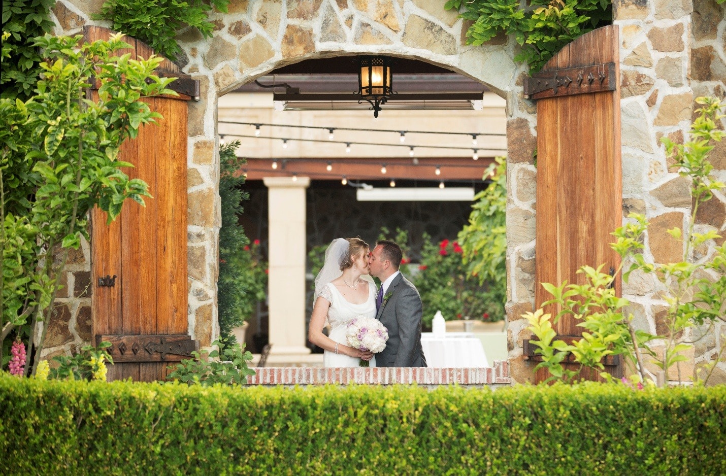 A bride and groom share a kiss under a stone archway in Wine Country
