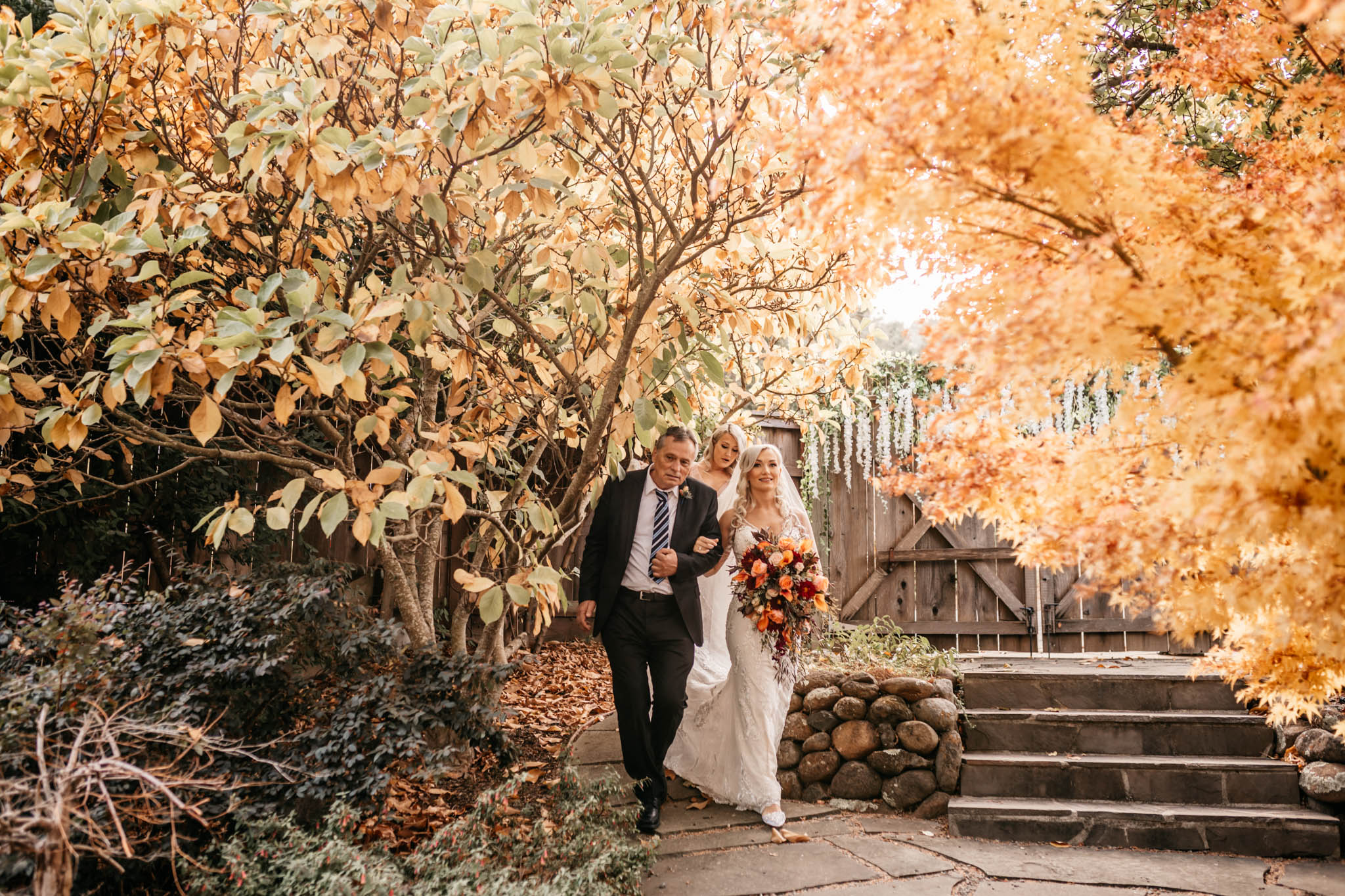 A bride and groom walk a golden autumn path on their wedding day